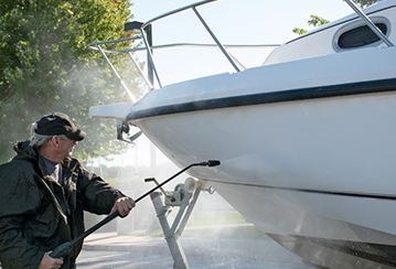 Older man power washing boat mid-day