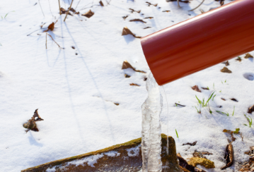 A drainspout has ice flowing out the bottom onto snowy ground.