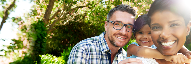Three people stand outdoors in a garden setting smiling at the camera