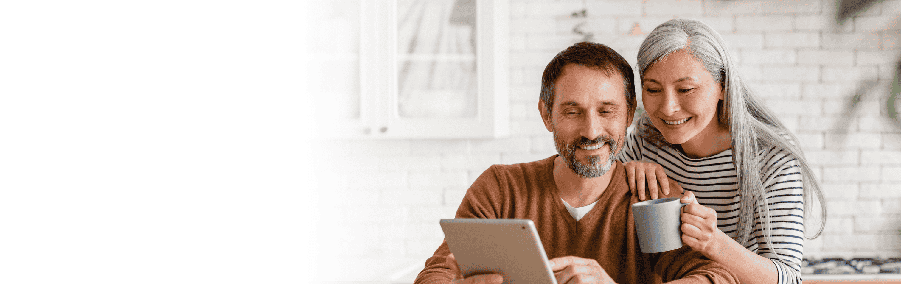 Man holding tablet and woman holding mug in home kitchen